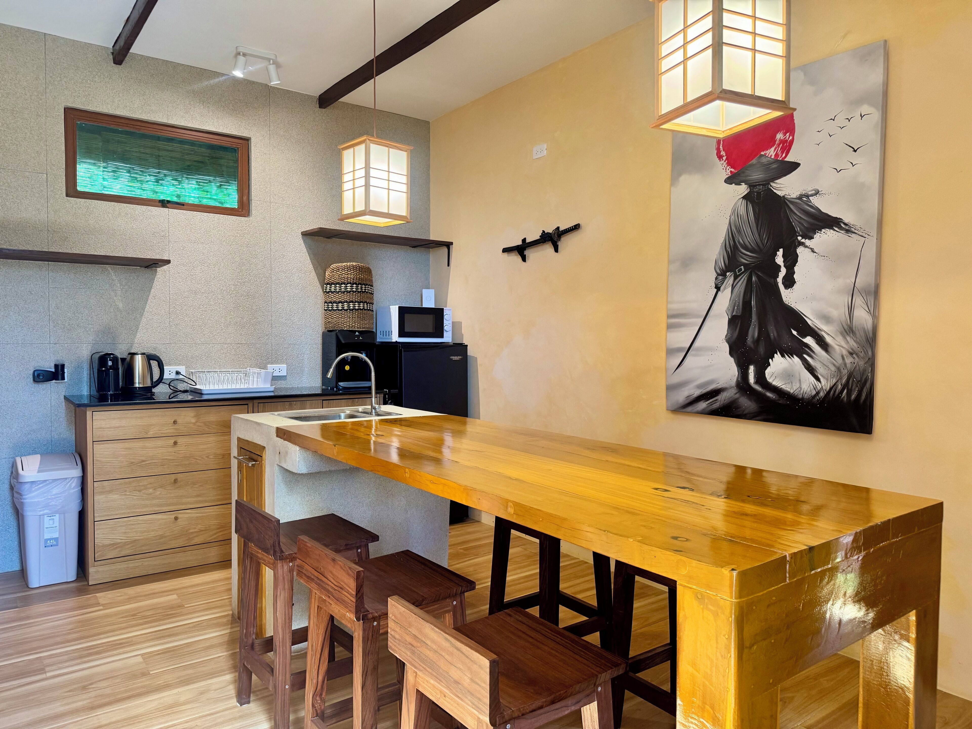 Une cuisine moderne avec un bar en bois et des tabourets, un four à micro-ondes, une machine à café et un tableau accroché au mur.