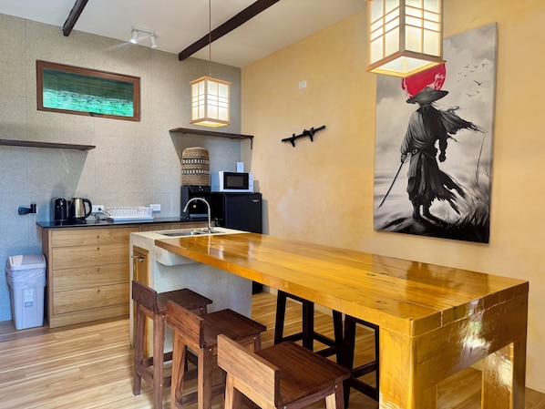 A modern kitchen with a wooden bar and stools, a microwave, a coffee maker, and a painting on the wall.