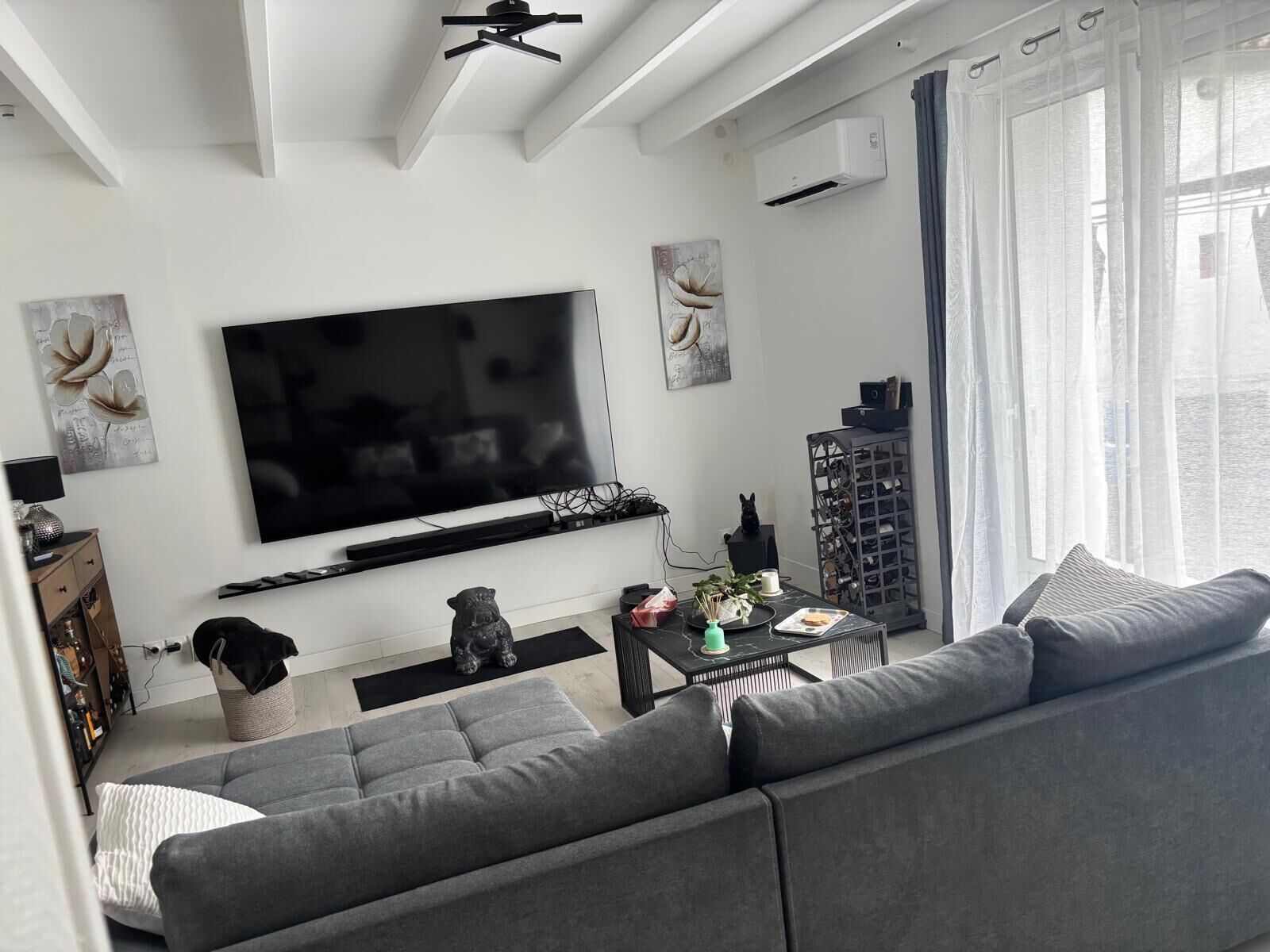 Un salon moderne doté d’un grand téléviseur à écran plat, d’un canapé gris et d’une table basse agrémentée d’objets décoratifs.