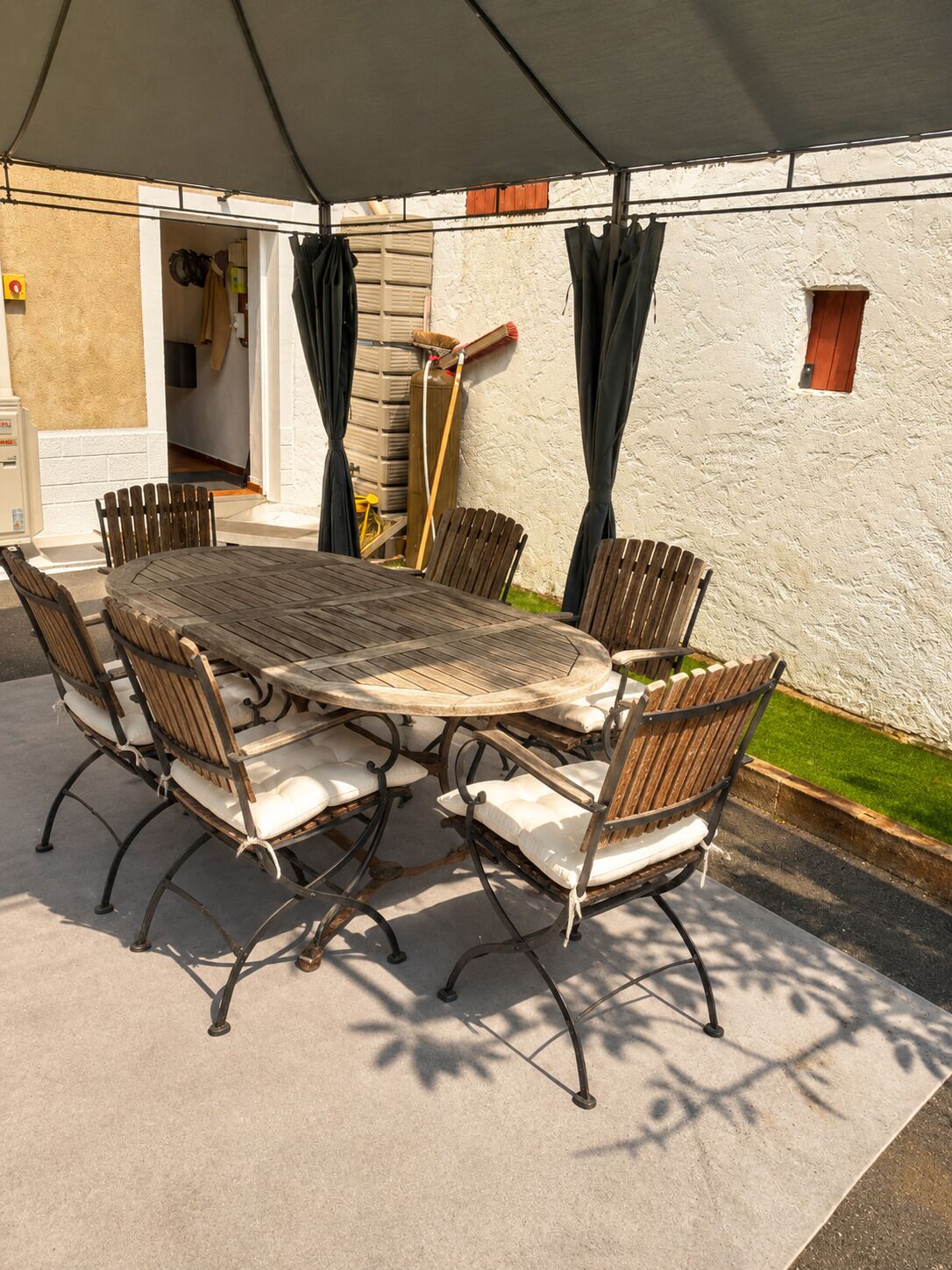 Un espace de restauration en plein air avec une table ronde et six chaises, entouré d’un mur blanc et d’une partie abritée.