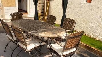 Un espace de restauration en plein air avec une table ronde et six chaises, entouré d’un mur blanc et d’une partie abritée.