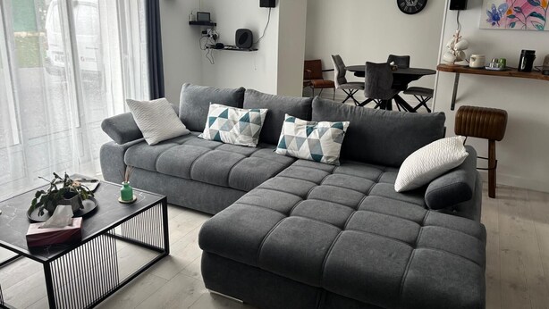 A modern living room with a grey sofa, a coffee table, and a dining area in the background.