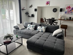 Ein modernes Wohnzimmer mit einem grauen Sofa, einem Couchtisch und einem Essbereich im Hintergrund.