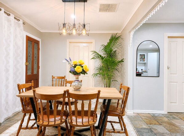 A dining area with a wooden table and chairs, a vase with flowers, and a large plant.