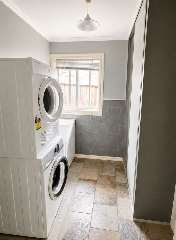 A laundry room with a washing machine, dryer, and a window with blinds.