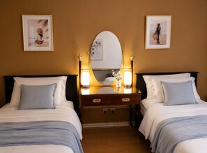 A hotel room with two beds, a wooden dresser with a mirror, and framed artwork on the walls.