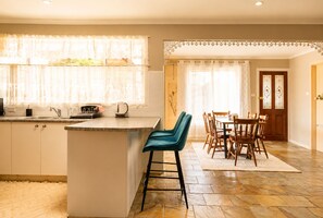 A kitchen with a central island, bar stools, a dining area with wooden chairs, and a patterned rug.