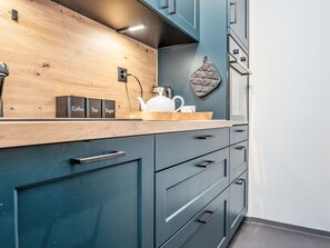 Eine Küche mit dunkelblauen Schränken, einer Holz Arbeitsplatte und einem Wasserkocher.
