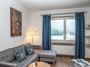 Ein Wohnzimmer mit grauem Sofa, einer Lampe, einem Fenster mit Vorhängen und einem Gemälde an der Wand.