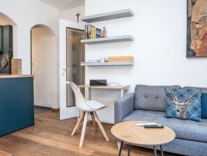 Un saló modern amb un sofà gris, una taula de centre rodona de fusta, una cadira blanca i una biblioteca amb llibres i objectes decoratius.
