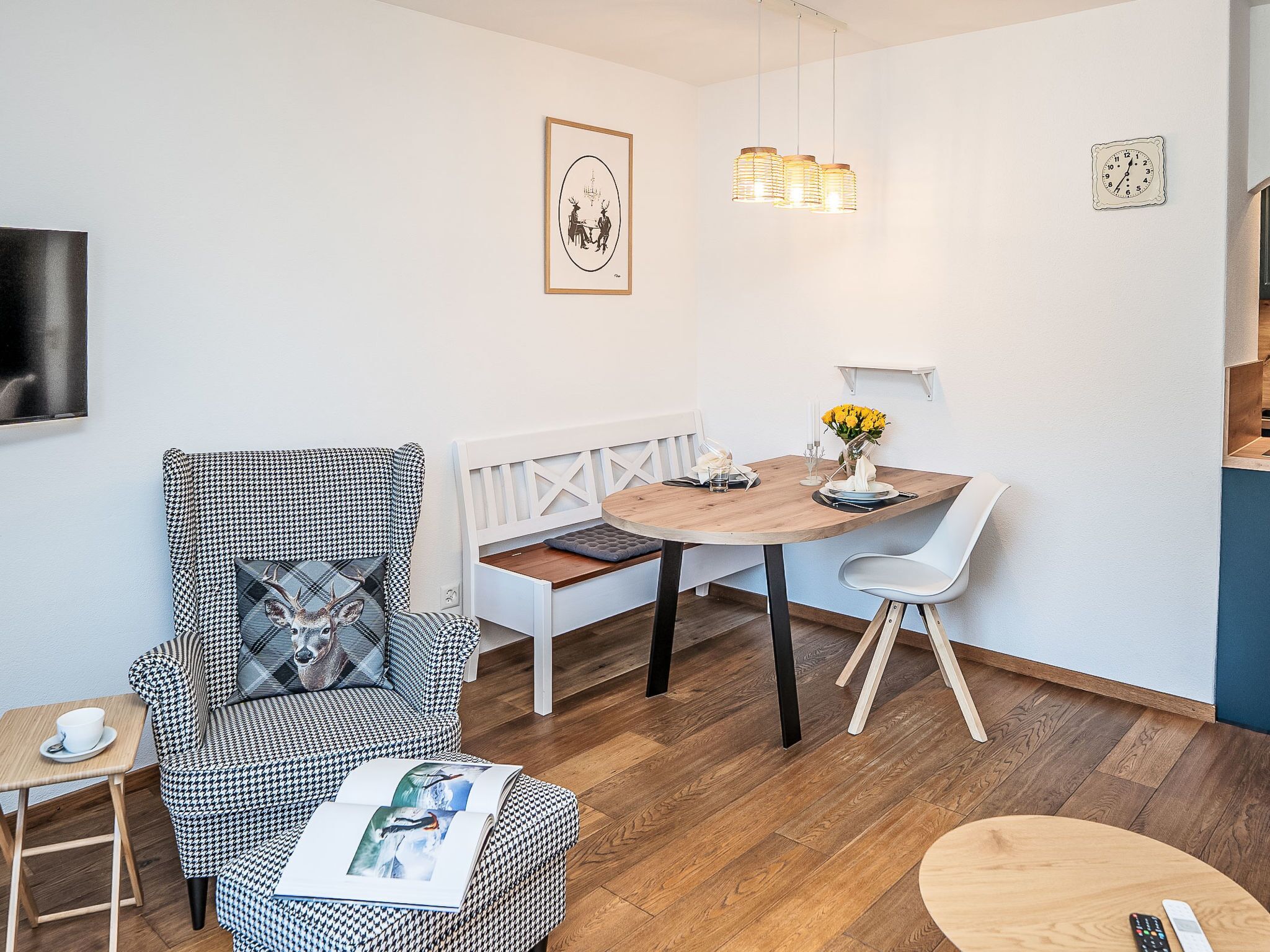A modern living room with a houndstooth patterned armchair, a wooden dining table with white chairs, a bench, and a small side table with a cup.
