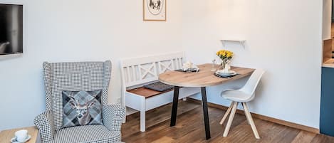 A modern living room with a houndstooth patterned armchair, a wooden dining table with white chairs, a bench, and a small side table with a cup.