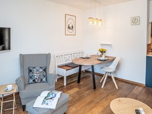 Ein modernes Wohnzimmer mit einem hundszahn-gemusterten Sessel, einem Holzesstisch mit weißen Stühlen, einer Bank und einem kleinen Beistelltisch mit einer Tasse.