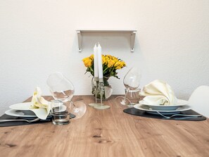 Ein Esstisch, gedeckt mit Tellern, Besteck, Gläsern und einer Mittelstück aus gelben Blumen und Kerzen.