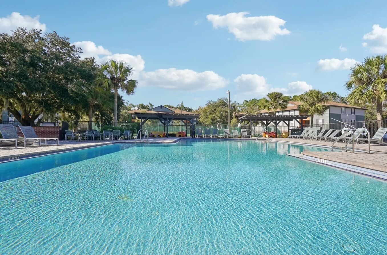 A clear swimming pool with lounge chairs and a gazebo in a sunny outdoor setting.
