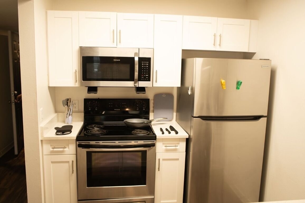 A compact kitchen with white cabinets, a stainless steel microwave, oven, and refrigerator.