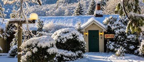A snow-covered landscape with a small building labeled 'OFFICE' in the foreground, surrounded by snow-laden trees and a clear sky.