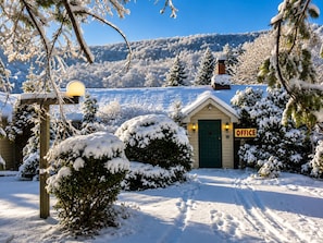 A snow-covered landscape with a small building labeled 'OFFICE' in the foreground, surrounded by snow-laden trees and a clear sky.