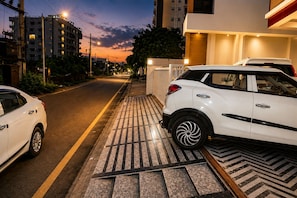 A street view at dusk with a white car parked on the side, buildings in the background, and a clear sky. - Hotel Aura (Jaipur)