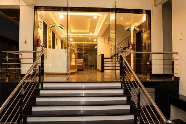 Un vestíbulo de hotel con un mostrador de recepción, una escalera con barandillas metálicas y una entrada de cristal.
