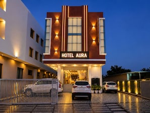 A hotel with a modern facade, a sign reading 'HOTEL AURA,' and a gated entrance with parked cars. - Hotel Aura (Jaipur)