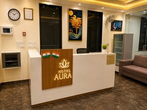 A hotel reception desk with a clock, framed certificate, and artwork on the wall. - Hotel Aura (Jaipur)
