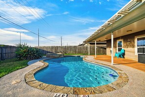 A swimming pool with a wooden deck surrounding it, a wooden fence in the background, and a building with a covered patio area. - Private Pool + Spa + Fenced Backyard • Near North Padre Island | Graceland (Corpus Christi)