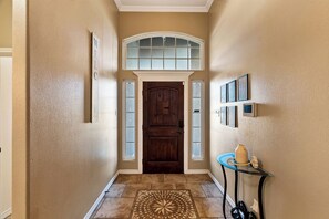 Un pasillo con puerta de madera, ventanal encima y suelo de baldosas.