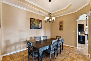 A dining area with a dark wooden table and chairs, a chandelier, and artwork on the walls. - Private Pool + Spa + Fenced Backyard • Near North Padre Island | Graceland (Corpus Christi)