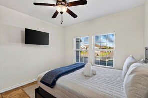 A bedroom with a bed, a ceiling fan, a TV, and a window with blinds. - Private Pool + Spa + Fenced Backyard • Near North Padre Island | Graceland (Corpus Christi)