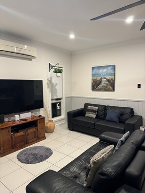 A modern living room with a flat-screen TV, a black leather sofa, a wooden entertainment unit, and a painting on the wall.