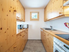 A compact kitchen with wooden cabinets, a microwave, a sink, and a dishwasher. - Collina 5i-02 by Interhome (Flims)