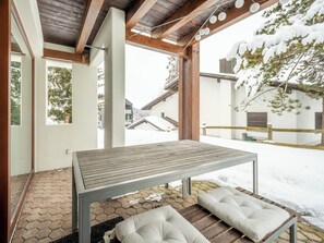 A covered outdoor seating area with a table and benches, a wooden ceiling, and a view of a snowy landscape. - Collina 5i-02 by Interhome (Flims)