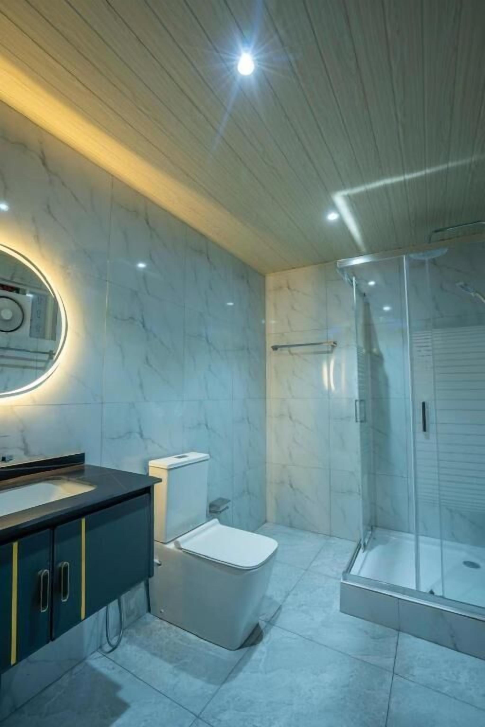 A modern bathroom with a marble wall, a toilet, a sink with a mirror, and a glass-enclosed shower.