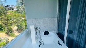A modern bathroom with a bathtub, a shower, and a window offering a view of the outdoors.