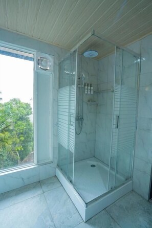 Een douche met glazen wanden, een witte betegelde vloer en een raam aan de zijkant.