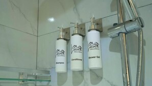 A bathroom with a marble floor, a glass shelf, and three white bottles labeled with a brand name and product types.