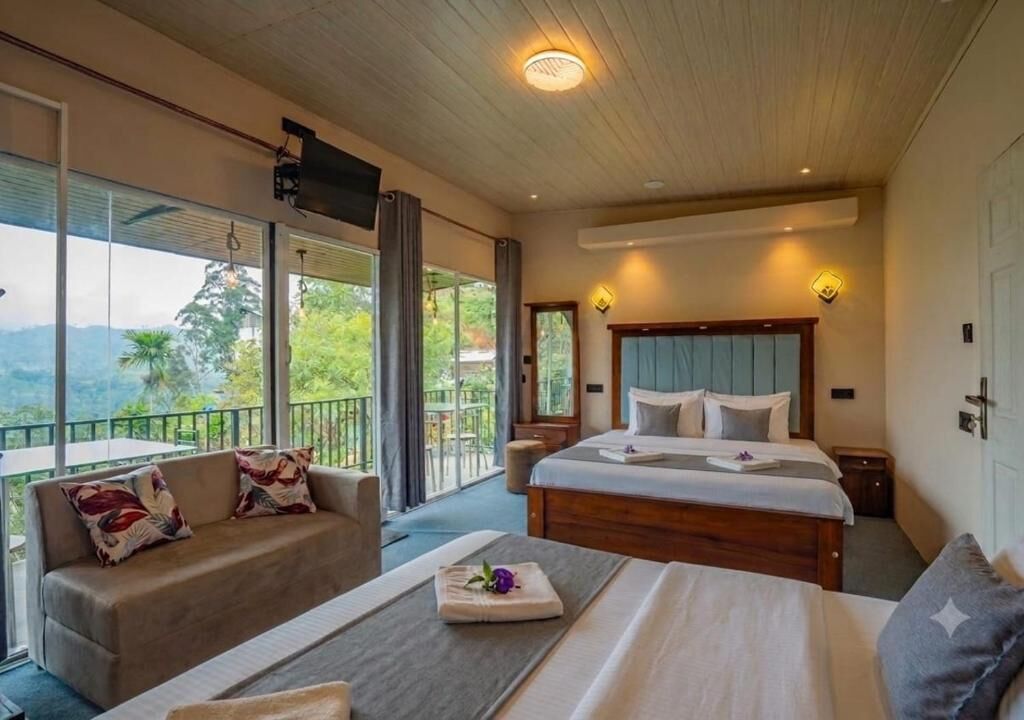 A hotel room with a large bed, a sofa, a small table, and a balcony with a view of the outdoors.