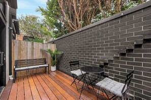 A wooden deck with a bench and two chairs, a brick wall, and a potted plant.