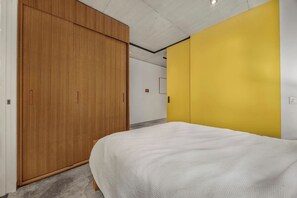 A bedroom with a bed, a wooden wardrobe, and a yellow accent wall.