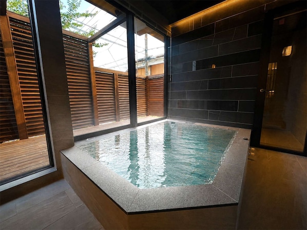 Una piscina interior moderna con cerramiento de vidrio, cubierta de madera y paredes de baldosas oscuras.