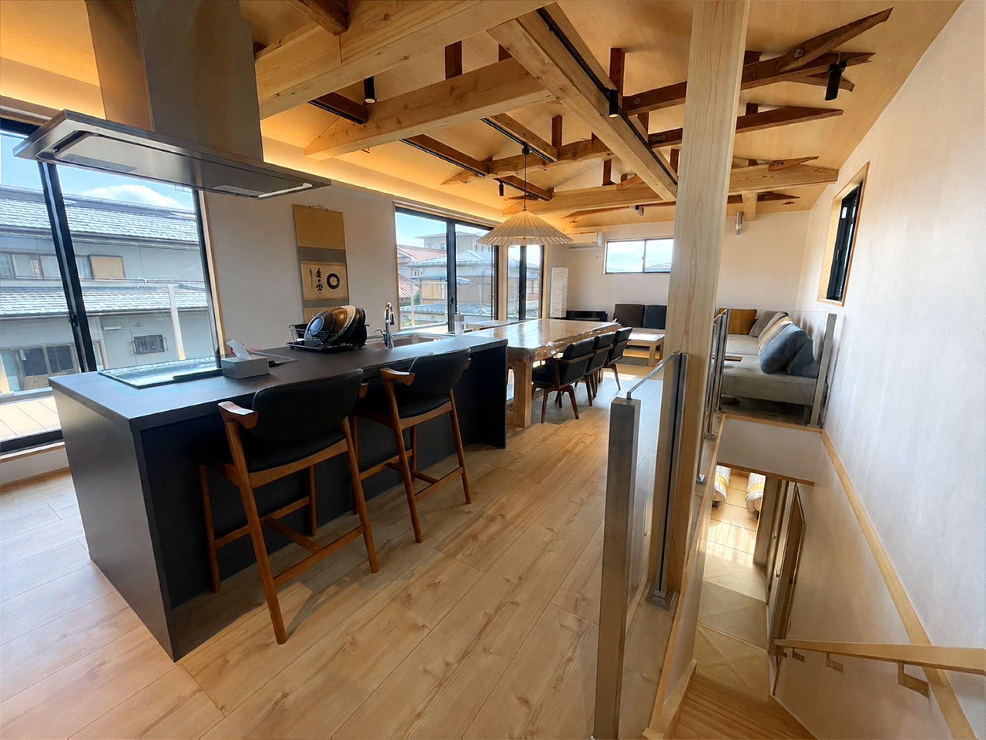 A modern kitchen with a bar area, wooden beams, and large windows.