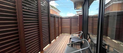 A covered outdoor deck with wooden flooring and metal chairs.