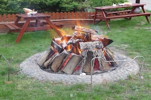 Ein Lagerfeuer mit Holzscheiten, umgeben von einer Steingrenze, und ein Holztisch im Hintergrund.