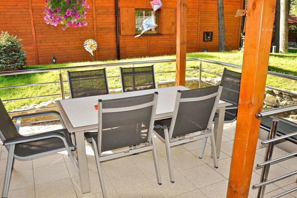 Ein Sitzbereich im Freien mit Tisch und Stühlen, ein Holzgebäude im Hintergrund und eine hängende Blumenampel.
