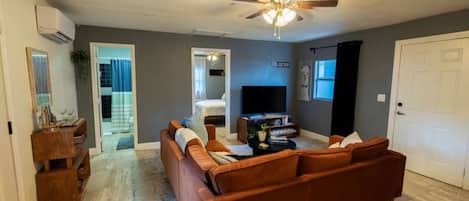 Een woonkamer met een bruine bank, een plafondventilator, een flatscreen-tv en een deur met de tekst 'GUEST ROOM'.