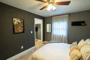 Ein Schlafzimmer mit einem Bett, einem Deckenventilator, einer Tür zu einem Schrank und einem Fenster mit Vorhängen.