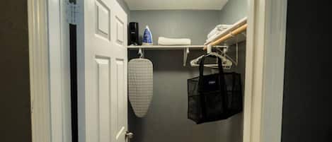 A narrow hallway with a door, a hanging ironing board, and a shelf with various items.