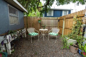 Un espace patio avec deux chaises en métal blanc, une petite table ronde et une clôture en bois.