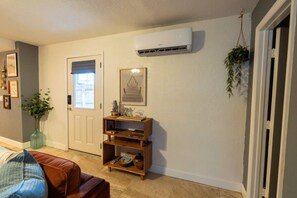 Ein Wohnzimmer mit weißer Tür, einer Wand-Klimaanlage, einem Holzkonsolentisch mit Dekoration und einer hängenden Pflanze.